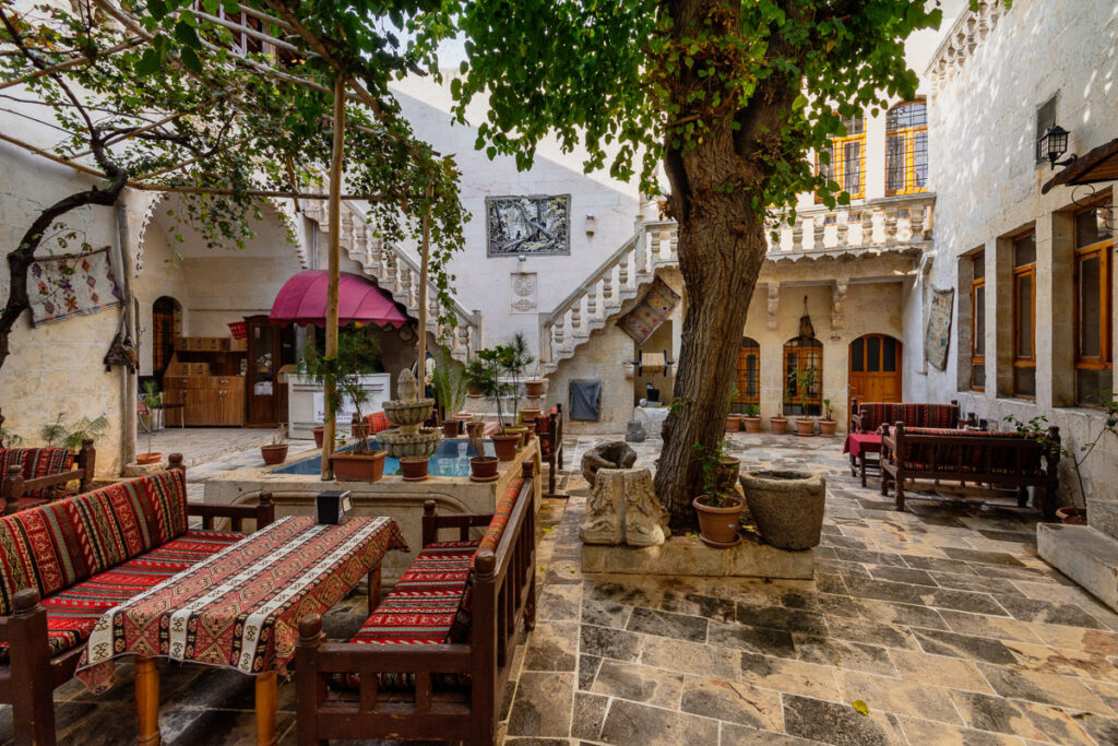 View of a hotel courtyard in SAnliurfa, a white traditional building with symmetric outside staircases, a shady tree and colourful tables and benches